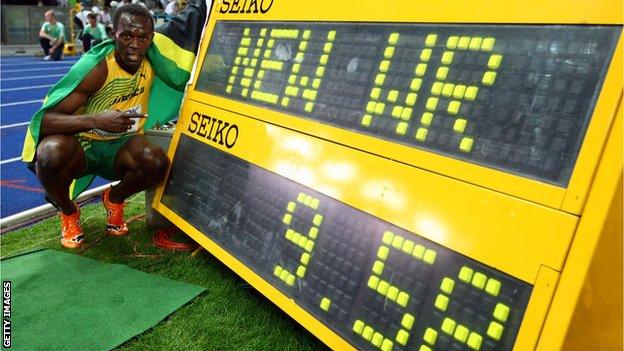 Usain Bolts poses next to the scoreboard showing his 100m world record