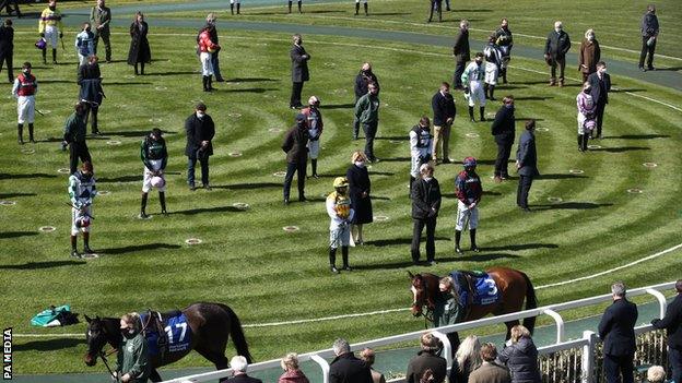 Trainers and jockeys stand in silence in the paddock at Aintree