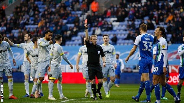 Referee Gavin Ward shows a red card to Wigan midfielder Kal Naismith in the 15th minute