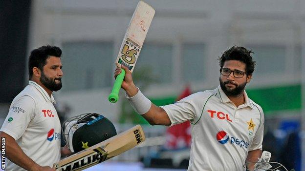 Pakistan batter Imam-ul-Haq (right) waves his bat to the crowd as he walks off with team-mate Azhar Ali (left) on day one of the first Test against Australia