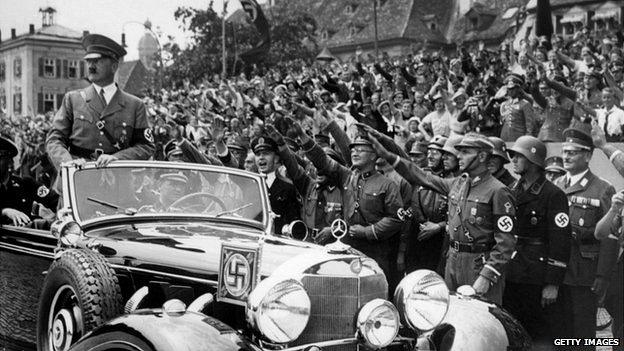 Adolf Hitler standing in a convertible Mercedes in front of a crowd in Germany, 1937