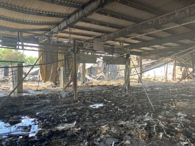 The skeleton of a building's ground floor is seen here, with only support pillars holding up the floor above on a blackened ground of ash