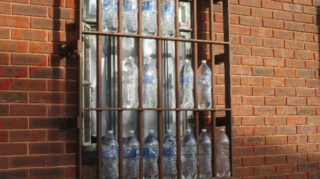 Fifteen plastic bottles outside a barred prison window, apparently ready to use for bottling hooch/illicit alcohol.