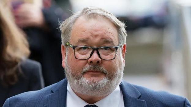 Close up of Christopher Mills outside court. He wears a blue suit, a white shirt and has black glasses. He has short grey hair and a grey beard.