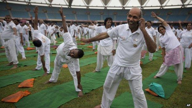 An Indian man attends to a call as he participates in a yoga session in the rain in New Delhi, India, Sunday, June 14, 2015