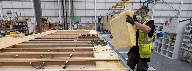 A man placing insulation material into the roof section of a modular house