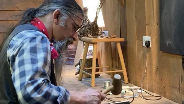 John Wills with a mallet in his hand in a workshop