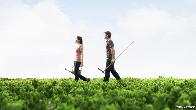 A man and woman walk through a field with gardening equipment