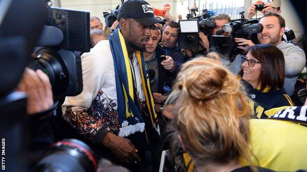 Usain Bolt, wearing a Central Coast Mariners scarf, is surrounded by fans, journalists and photographers after arriving in Sydney for his training period with the A-League side