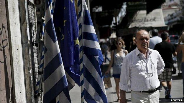 A man makes his way next to Greek national flags and a European Union flag in central Athens