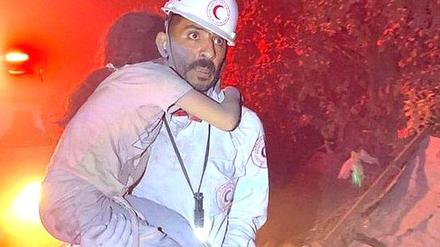 Paramedic Mohamed Mekkawy carries a girl through the street with an ambulance in the background