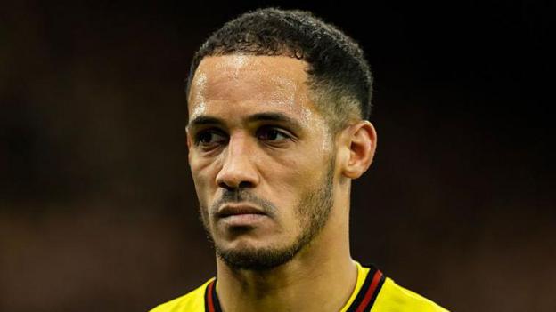 Tom Ince, wearing a yellow shirt with a red and black stripe while playing for Watford, looks on