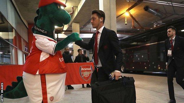 Mesut Ozil greeted by mascot Gunnersaurus before a Champions League tie against Paris St-Germain in 2016