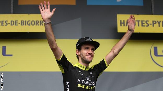 Simon Yates holds his hands up in celebration on the podium after winning stage 12