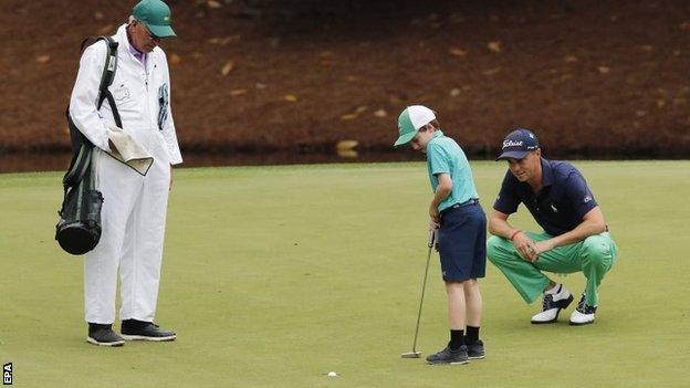 Justin Thomas watches a child hole his putt on the eighth