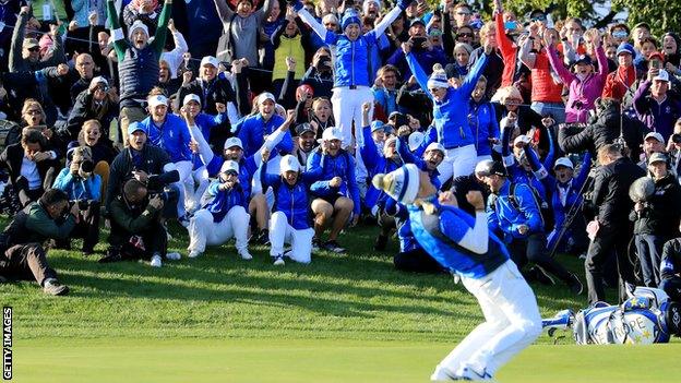 The European team rise to their feet along with supporters on the side of the 18th green as Pettersen celebrates