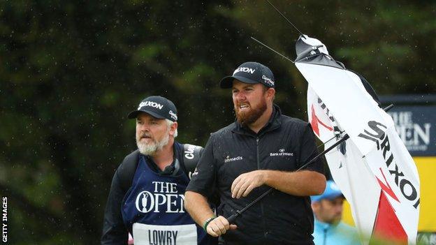 Shane Lowry stands with a broken umbrella