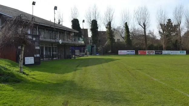 King George V playing field in Guernsey. The grass is short and green to the near side of the shot. There is also a club house visible in the picture.