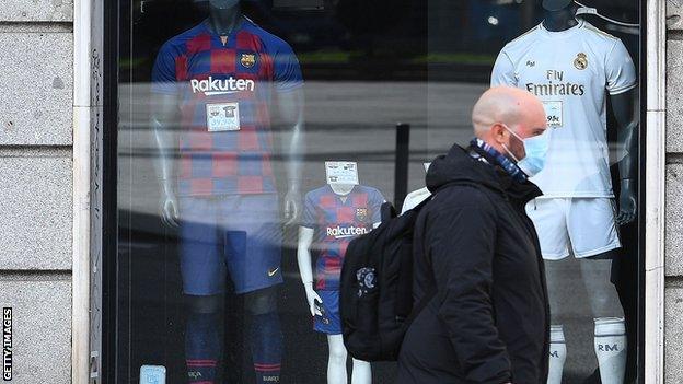 Member of the public wears a mask as he walks past Barcelona and Real Madrid shirts on sale