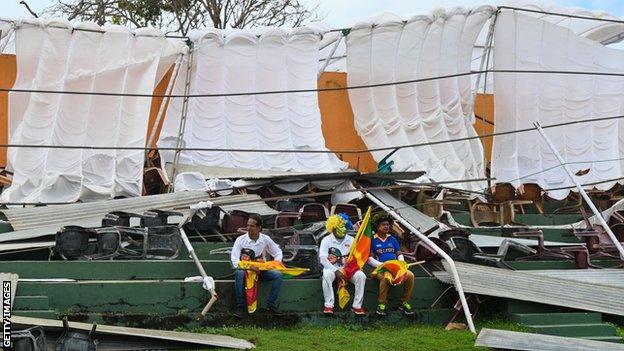 Spectators sit in front of a damaged stand in Galle