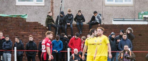 Fans watch from a broken wall at New Dundas Park