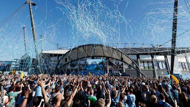 Manchester City fans watching on a big screen at Etihad Stadium celebrate their title success