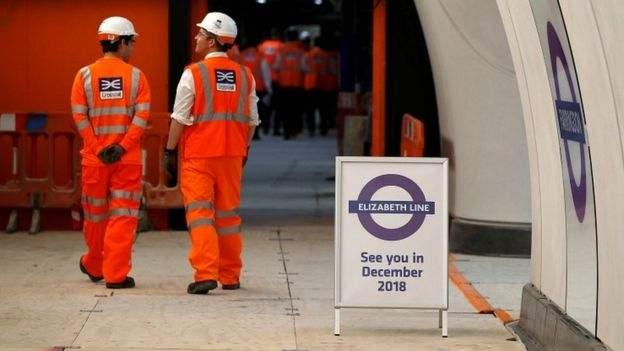 Crossrail workers stand near a sign saying "see you in 2018"