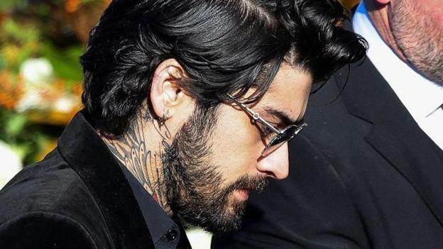 Zayn Malik pictured wearing black at Liam Payne's funeral - he is pictured from a side profile and has a visible tattoo on his neck, and is wearing sunglasses
