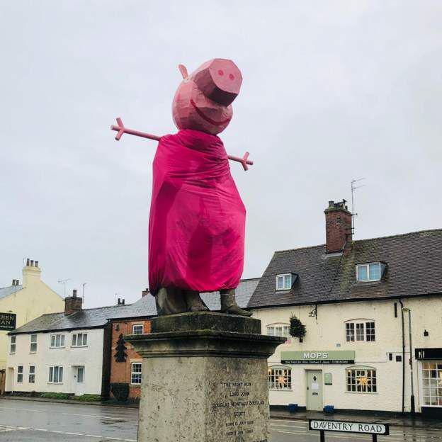 Statue with a pink costume on it, modelled Peppa Pig head and two outstretched arms.