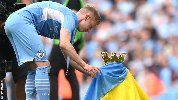 Manchester City's Oleksandr Zinchenko wraps a Ukraine flag around the Premier League trophy