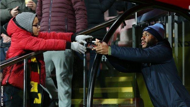 Raheem Sterling of Manchester City signs an autograph for a fan during the Premier League match between Watford FC and Manchester City at Vicarage Road on December 4, 2018 in Watford, United Kingdom