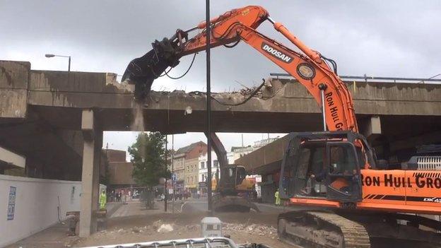 Machine prepares to knock down a bridge in the background