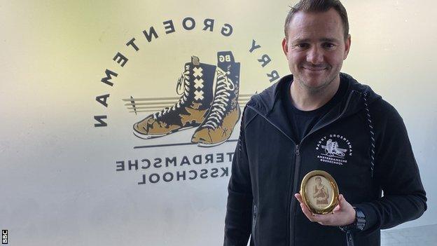 Barry Groenteman, posing with a framed portrait of Ben Bril, at his boxing gym in Amsterdam