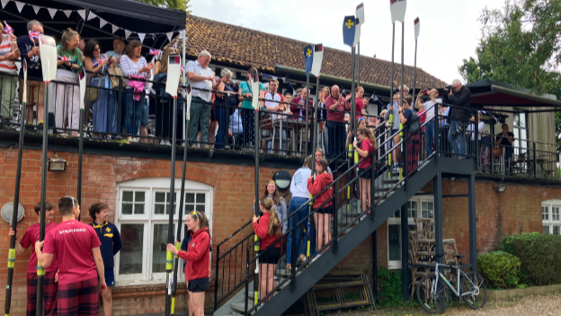 Dozens of people stand outside the clubhouse and line a staircase and clap as Esme Booth goes up the stairs