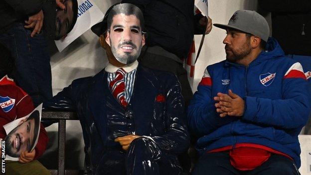 Carlos Gardel statue with a Luis Suarez mask at a Nacional game