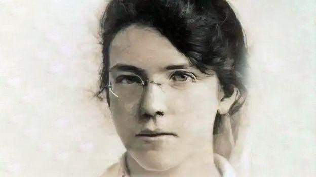 A grainy picture of Jane. She has dark hair which is tied up and is wearing glasses.