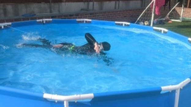 A girl in a wetsuit swims in a temporary pool in her back garden.