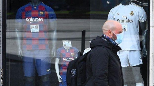 Man in mask walks past Barcelona and Real Madrid football shirts on sale