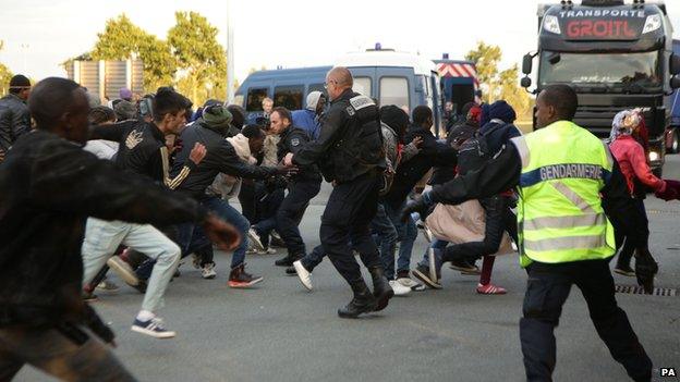 Migrants rush at a police cordon by a truck route along the perimeter fence of the Eurotunnel site at Coquelles in Calais, France on 30 July 2015