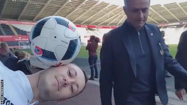 Jose Mourinho walks behind a gent balancing a ball on his head