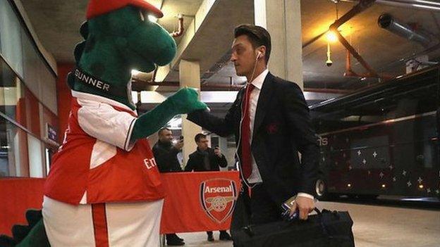 Mesut Ozil greeted by mascot Gunnersaurus before a Champions League tie against Paris St-Germain in 2016