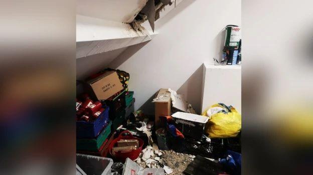 An attic with a hole in the plasterboard and rubble on the floor. There are bags and boxes.