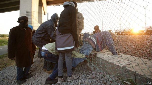 Migrants climb through a fence in Calais