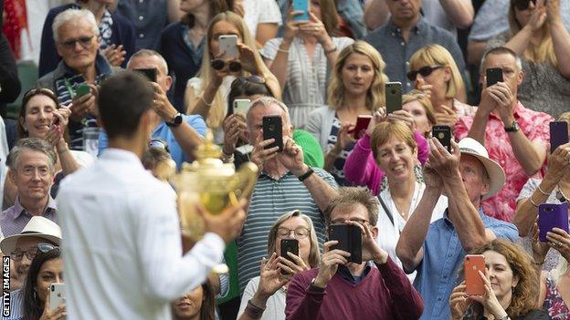 Serbia's Novak Djokovic shows off the men's singles trophy to fans after winning at Wimbledon in 2019