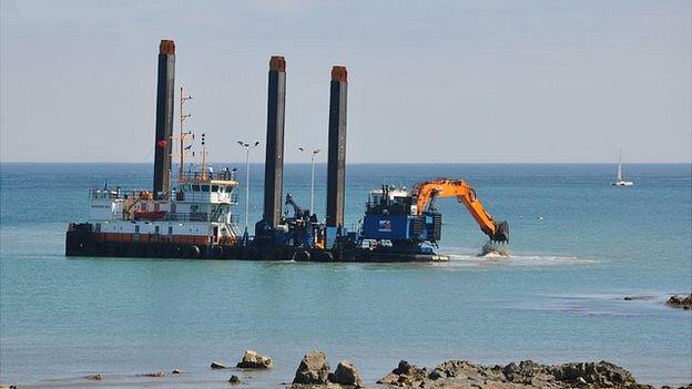 Digger working from a floating platform on the Guernsey sewage outfall pipe