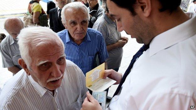 A bank employee checks the ID and bank booklet of a pensioner before enter a branch in the northern Greek port city of Thessaloniki, on 1 July