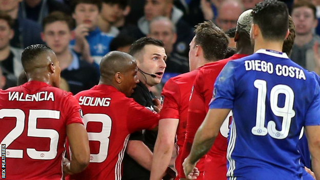 Referee Michael Oliver is surrounded by several Manchester United players after sending off midfielder Ander Herrera