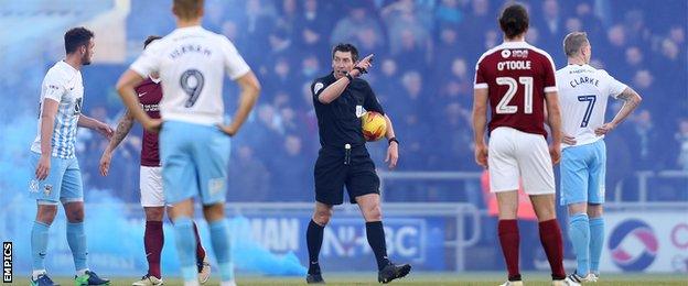 Referee Lee Probert instructs Northampton Town's and Coventry City's players to leave the pitch during the game as flares are thrown on to the pitch