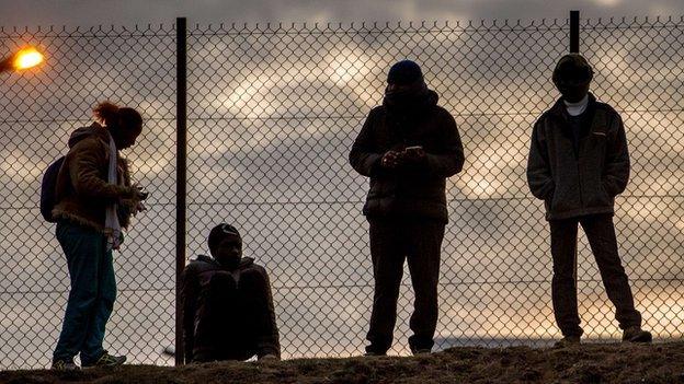 Migrants stand against a chain link fence inside the Eurotunnel site in Coquelles near Calais