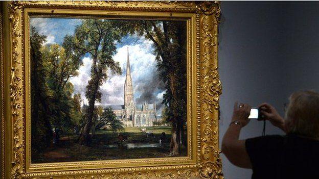 A woman photographs a painting by British artist John Constable entitled 'Salisbury Cathedral from the Bishops Grounds' 